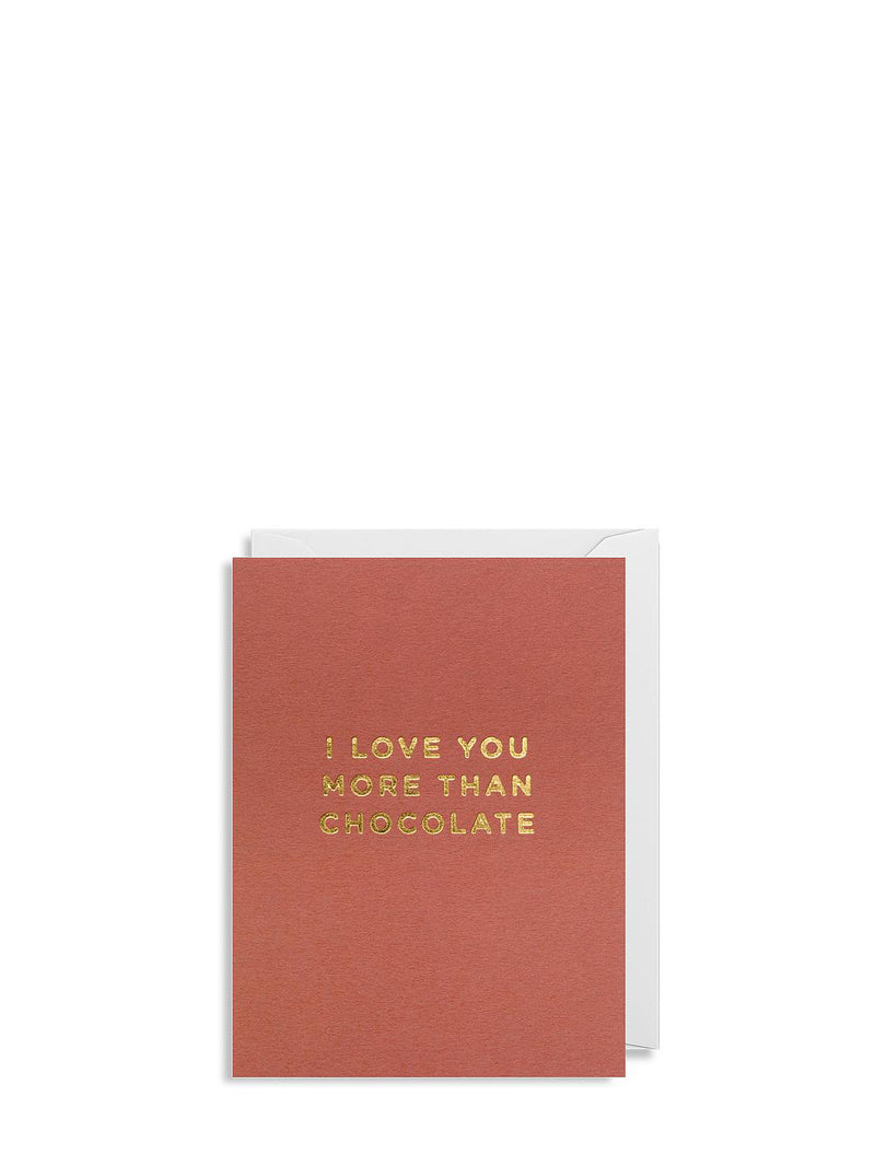 A solid colour brick-red mini greeting card with gold foil text 'I love you more than chocolate' on the front, accompanied by a white envelope.