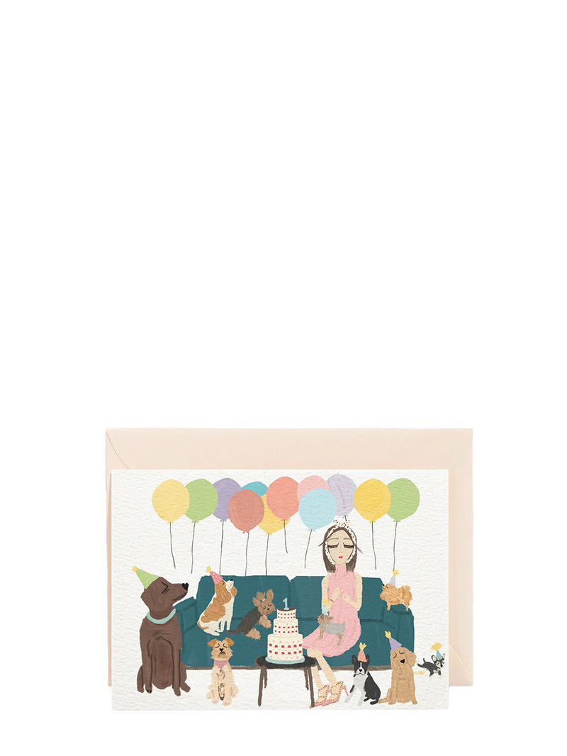 Illustrated card with a woman and dogs on a couch with balloons and a cake.