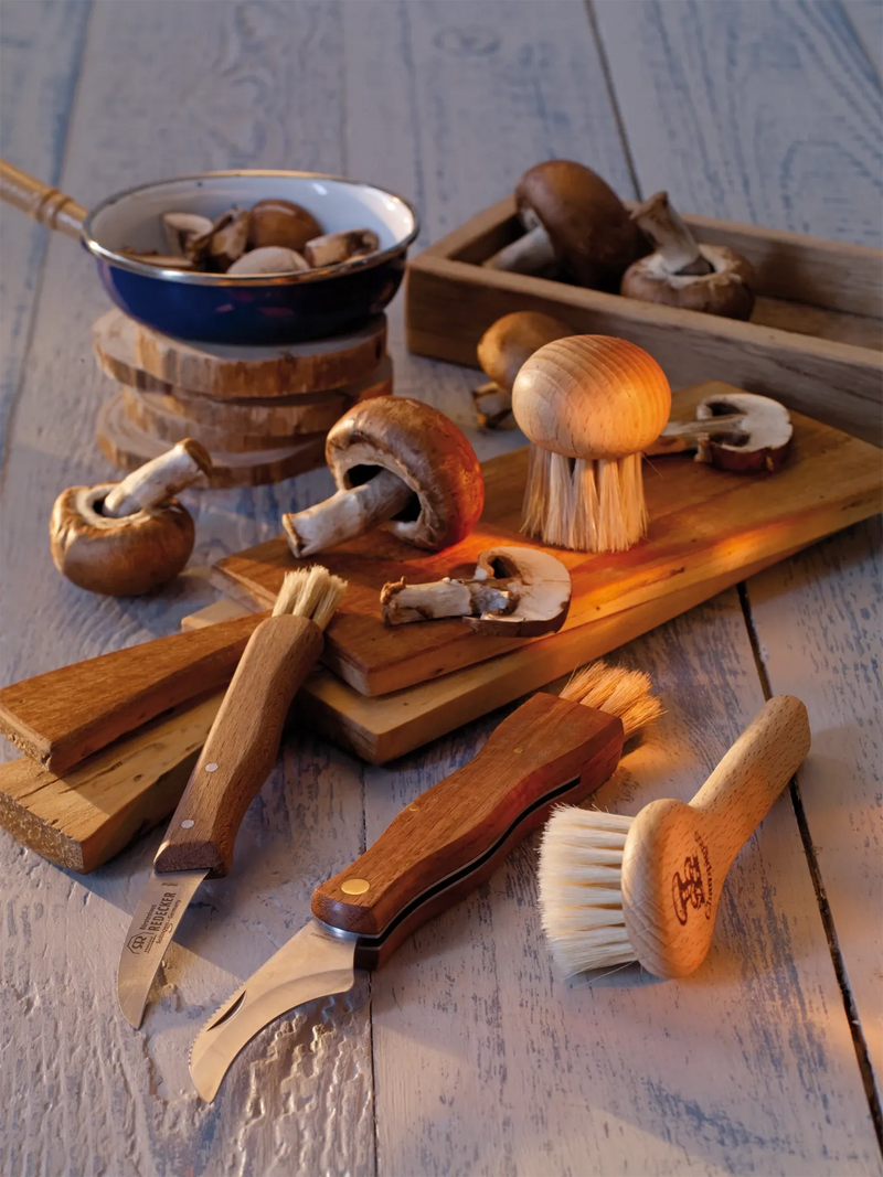 Wooden mushroom cleaning tools and a bowl of mushrooms on a wooden surface