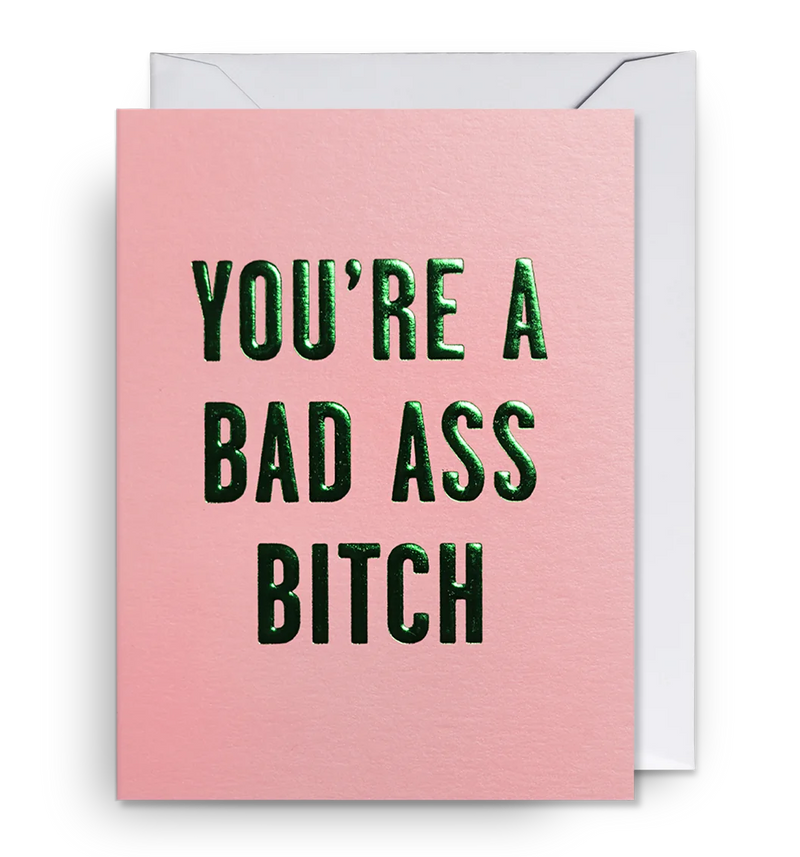 A pink mini greeting card with the text 'YOU'RE A BAD ASS BITCH' in green capital letters, accompanied by a white envelope.