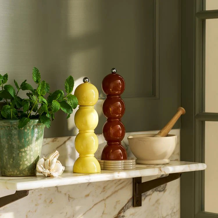 Decorative salt and pepper shakers on a marble shelf with a plant and mortar and pestle.