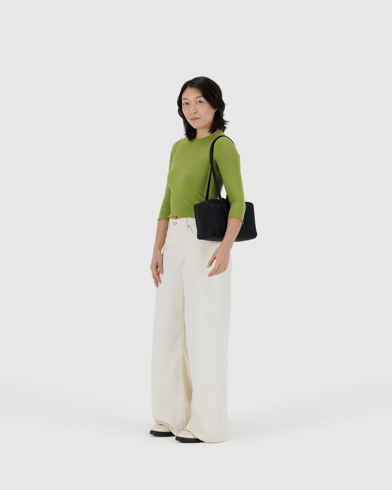 Woman wearing a green sweater and white pants holding a black handbag on a white background