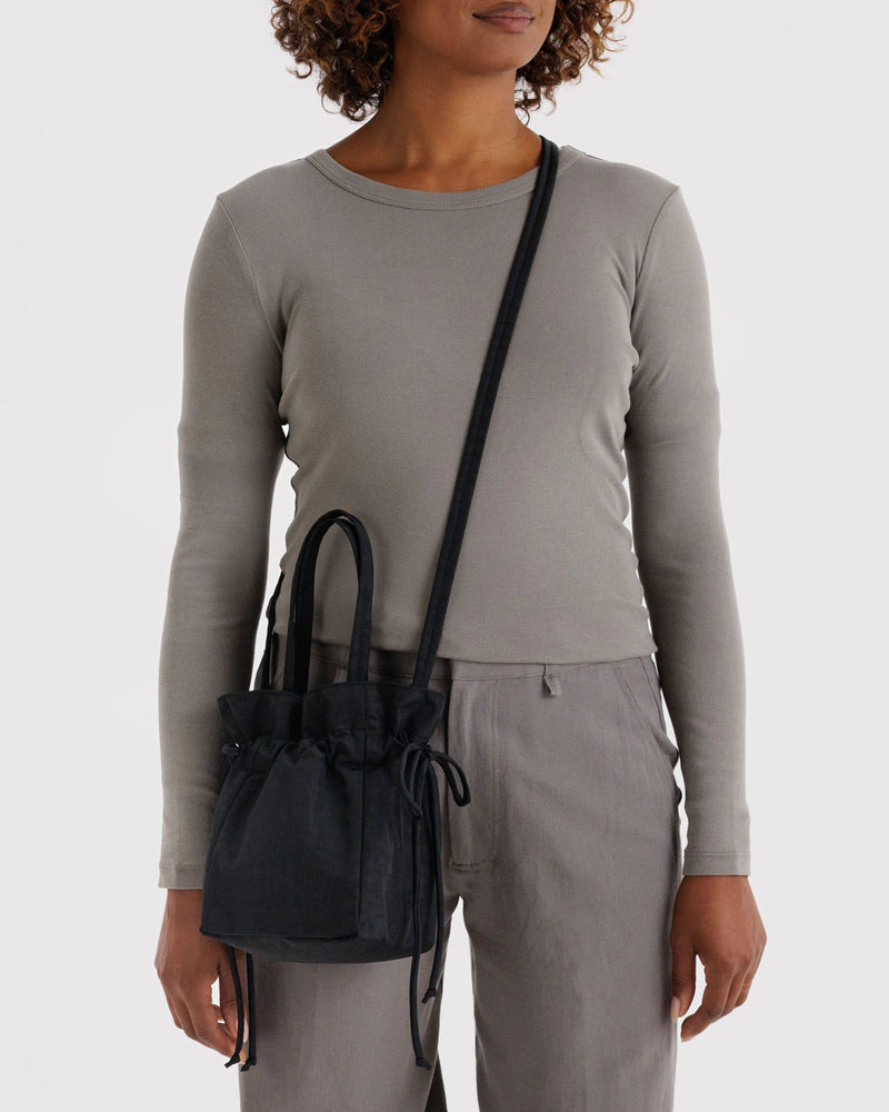 Person wearing a gray long-sleeve top and gray pants, holding a black handbag.