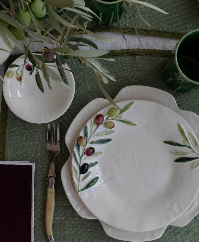 White ceramic plate with olive design on a green tablecloth with a fork and cup.