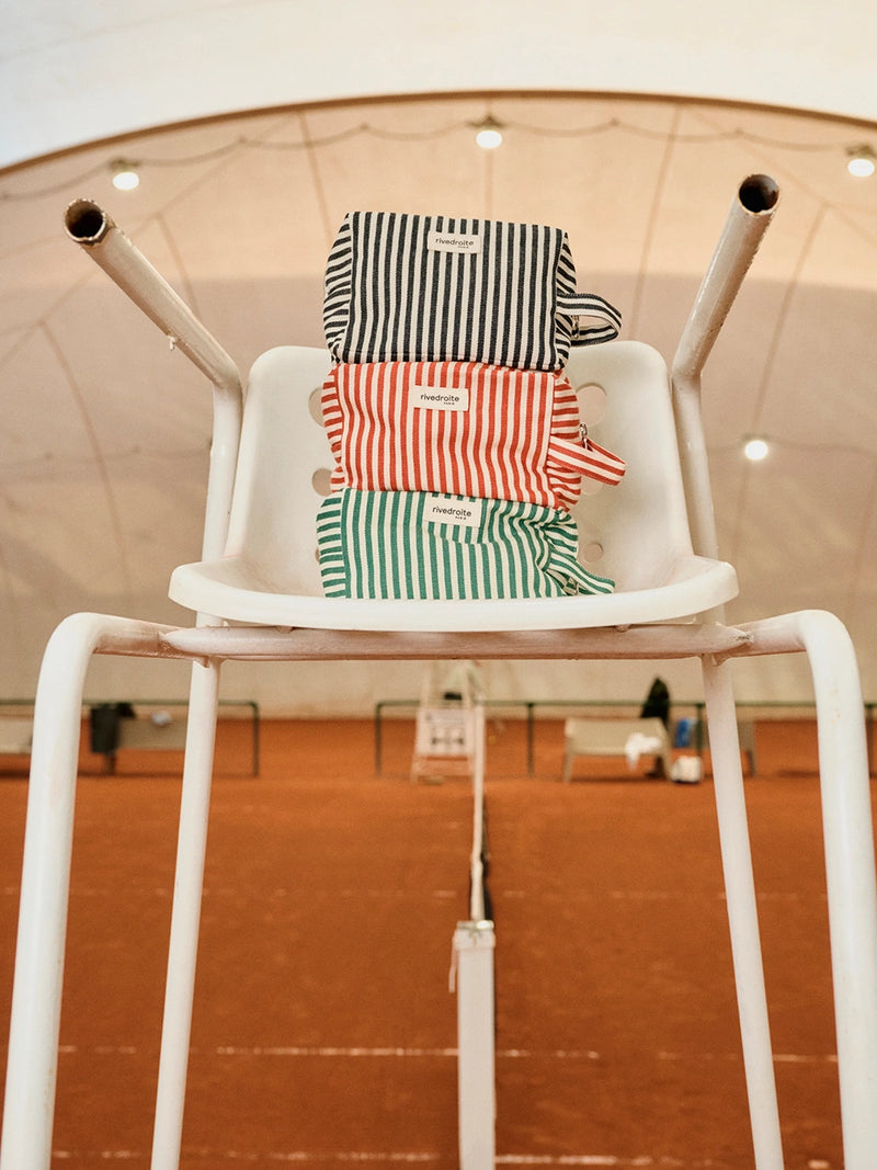 Three striped cosmetic bags stacked on a white chair with a blurred indoor background