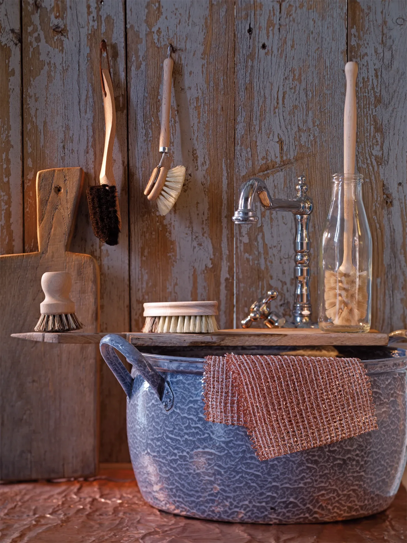 Vintage-style kitchen with ceramic sink, metal faucet, and cleaning brushes against a wooden wall.