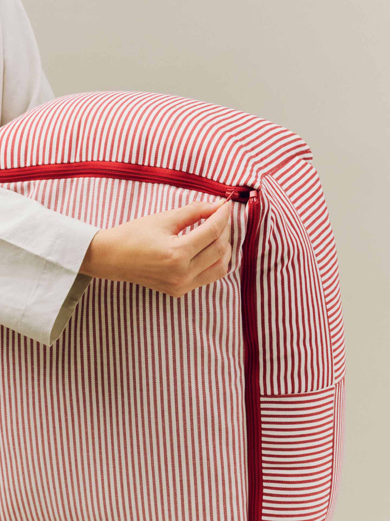 A close-up of a person's hand unzipping HAY's new dog bed with red and white vertical stripes and a red zipper at the bottom.