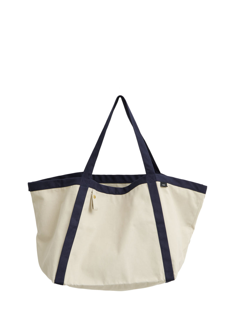 An off-white canvas tote bag with dark navy blue trim and handles, shown against a plain white background.