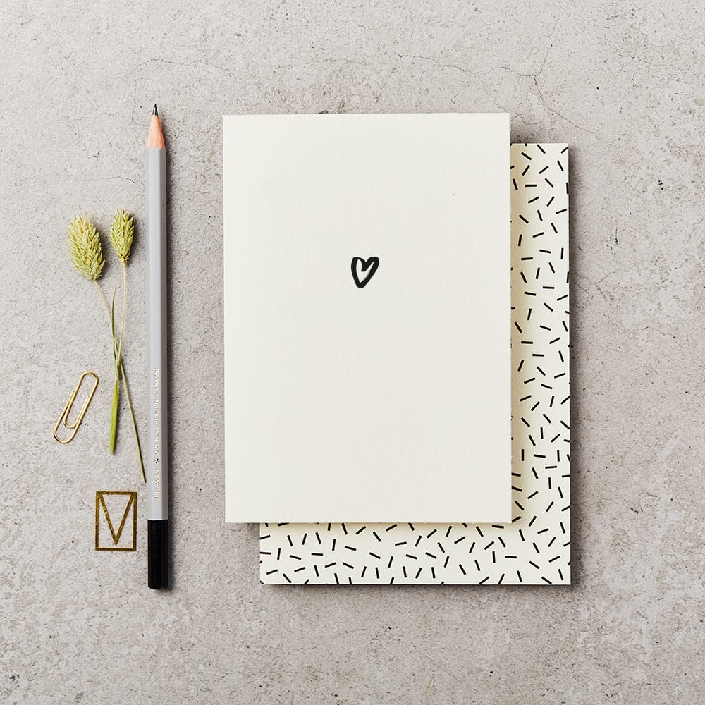 Love greeting card with a heart drawing, pencil, paper clips, and dried plants on a concrete surface