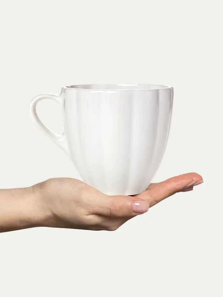 White ceramic mug held in a hand against a plain background