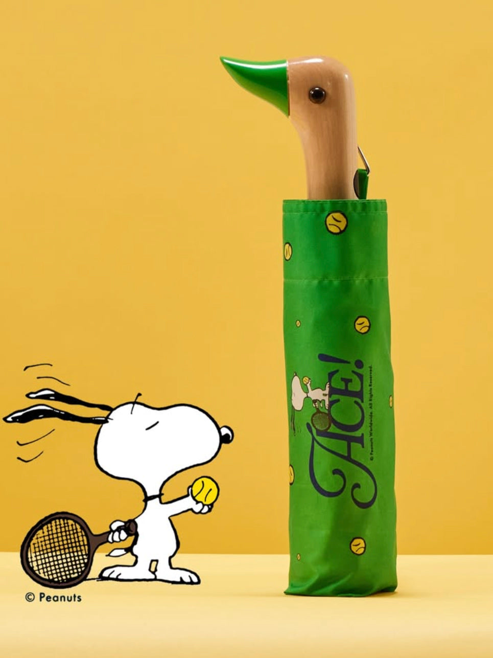 Green umbrella with Snoopy tennis player design on a yellow background
