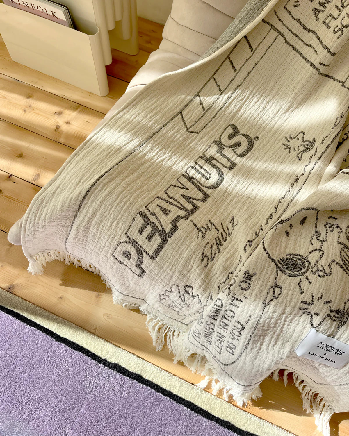 Beige blanket with 'PEANUTS' branding draped over a wooden surface.