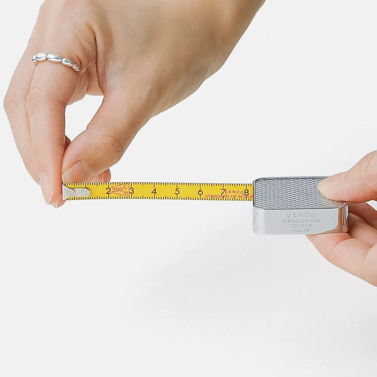Hand holding a small metal object next to a measuring tape on a white background