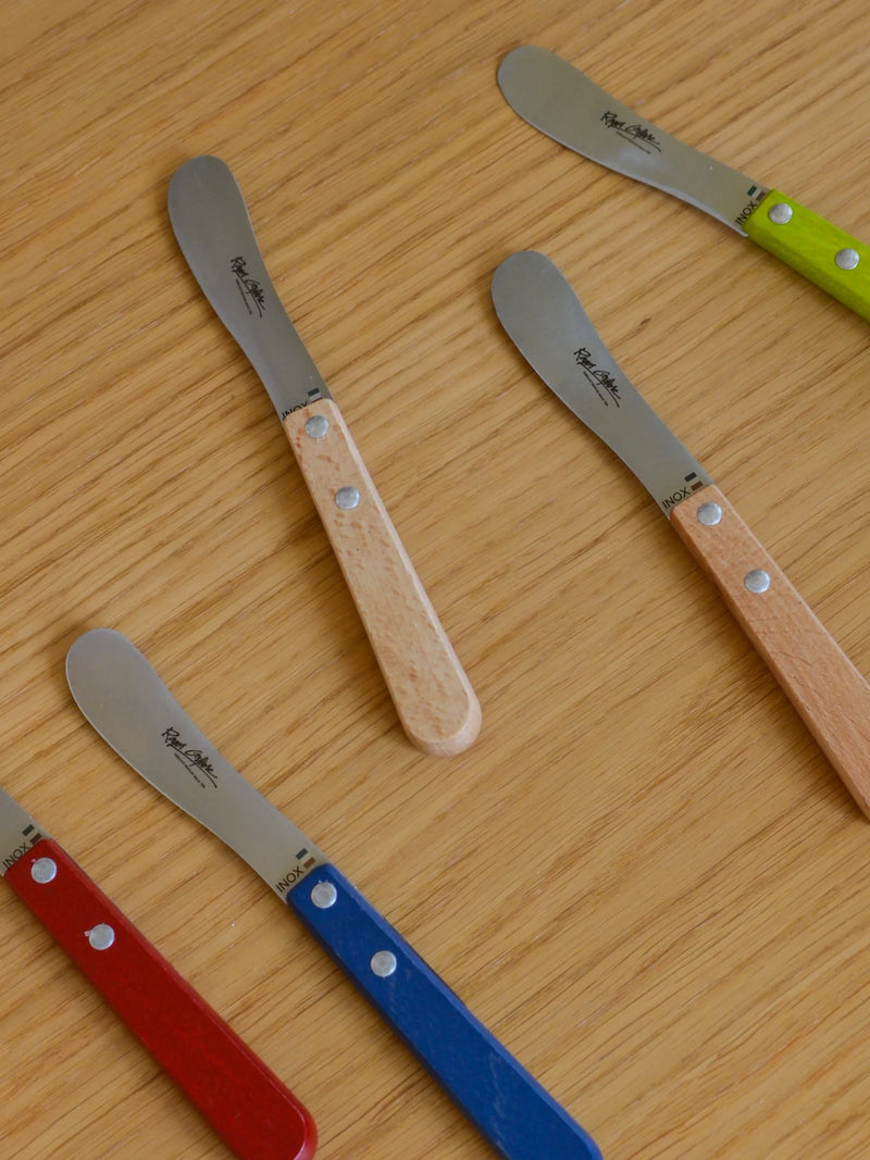 Set of four butter knives with different colored handles on a wooden surface