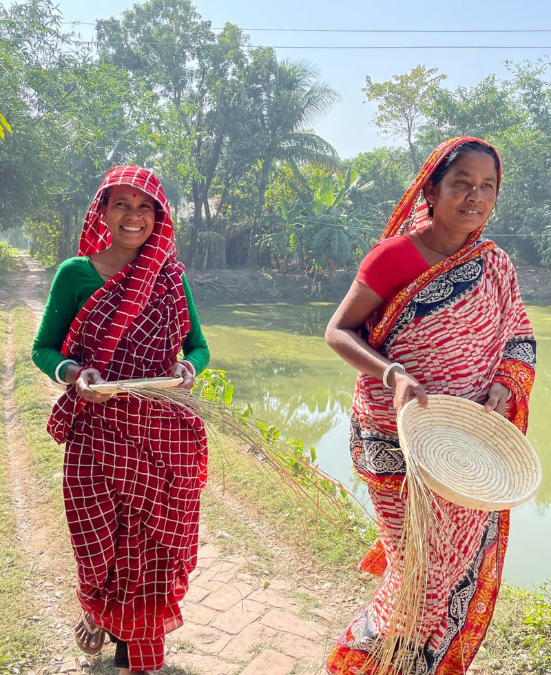 Two women in traditional attire standing outdoors with a natural background