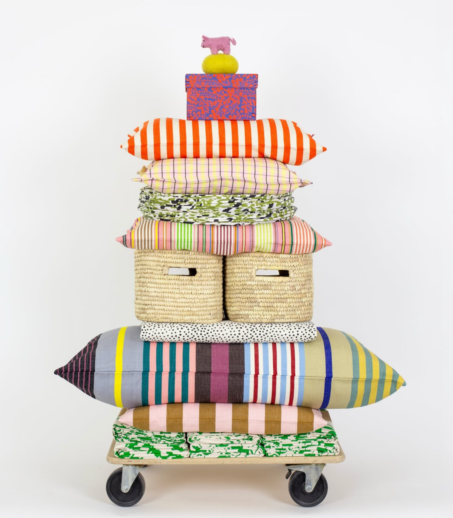 Stack of colorful pillows on a wheeled cart with a white background