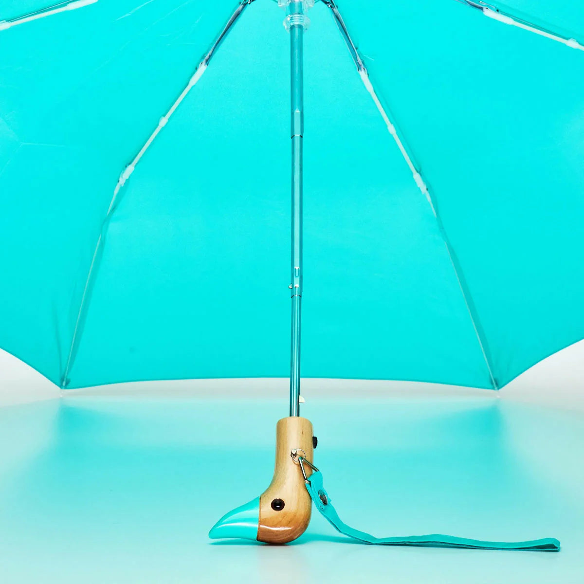 Turquoise umbrella with a wooden handle on a matching turquoise background