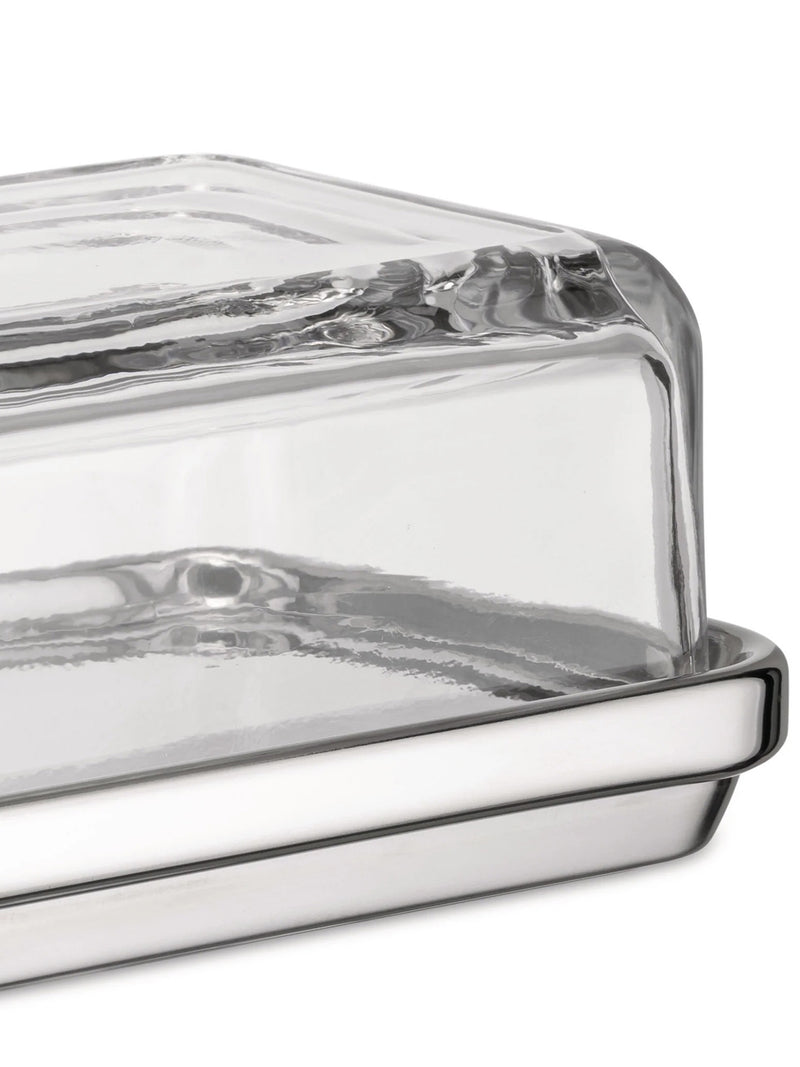 A close-up of a clear glass dish with a reflective silver metal base with a notched rim, photographed on a white background.