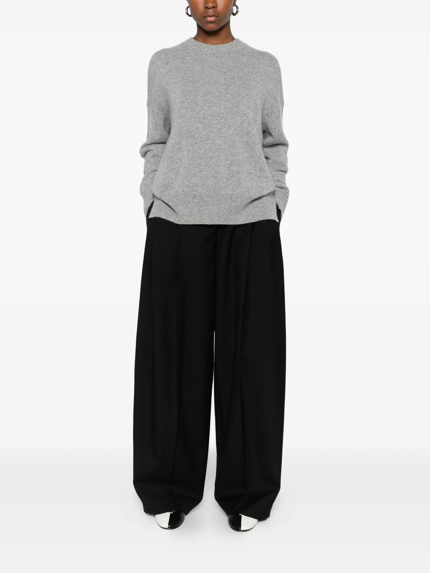 Person wearing a gray sweater and black pants on a white background