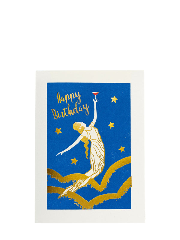 A square birthday card with a white border and a blue printed vintage-inspired design featuring a gold- and white toned female figure with long hair and classical draped dress, possibly a nymph or the spirit of the air or star, raising a glass of wine high above her head to the gold stars, while her other hand is bent in a graceful arch. She's flying or hoovering among wavy gold lines on the blue sky, and the words 'Happy Birthday' in gold script are spelled up in the corner