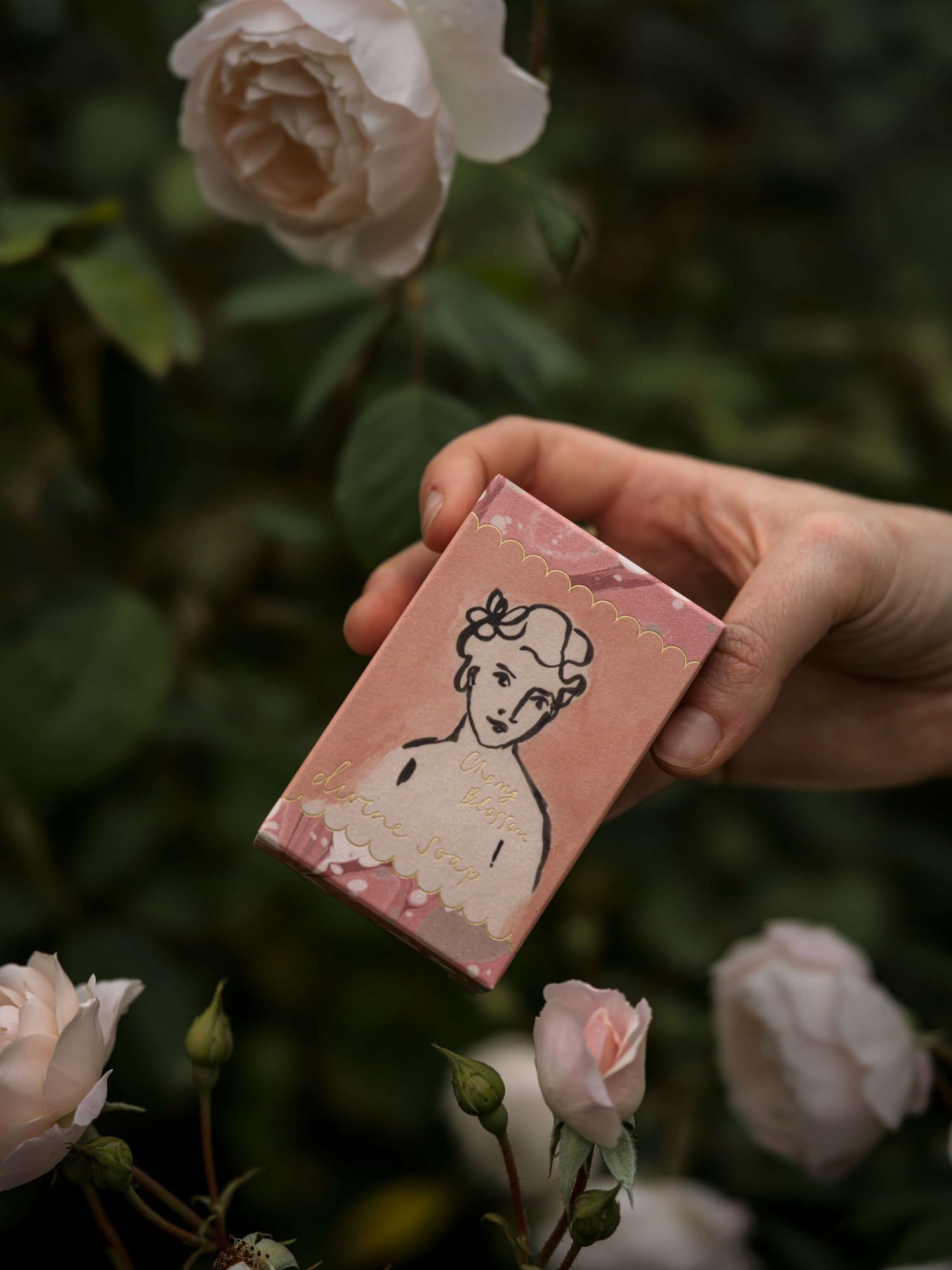 Hand holding a small pink box with a vintage illustration of a woman, surrounded by white flowers.
