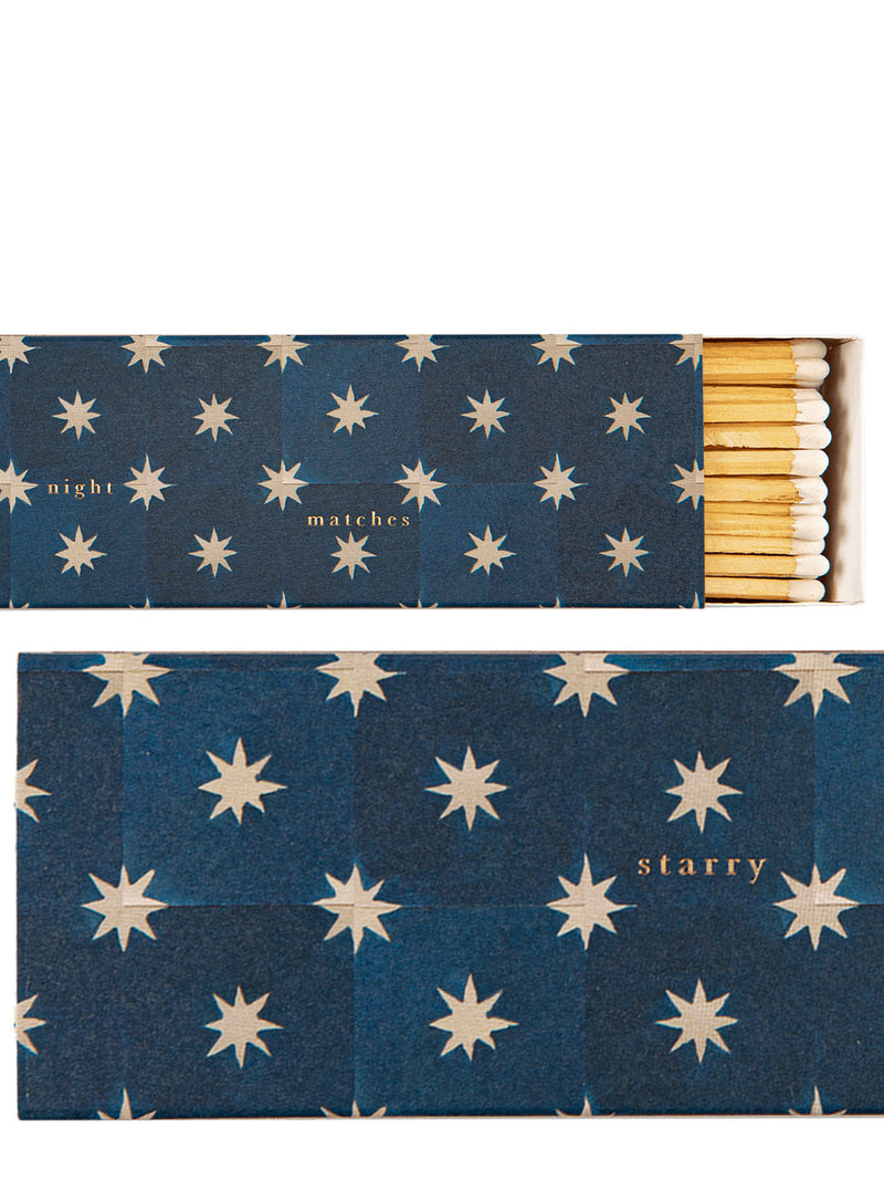 A close-ups of decorative matches with a dark blue cover patterned with little cream starbursts and gold print text. The top half shows the open matchbox with white-tipped wood coloured matches visible on the right side and the words 'night matches', and the bottom half shows the other end of the matchbox cover with the word 'starry' printed in gold.