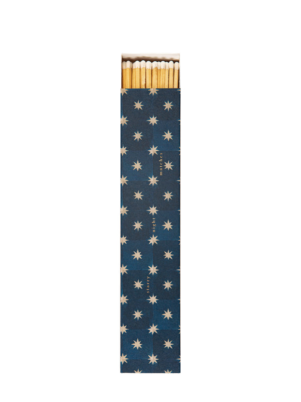 A long and thin match box with illustrated cover of geometric star pattern depicting a dark blue sky and white stars and the text starry night matches printed with small golden letters and the white-tipped match sticks visible from the top end, photographed against a white background