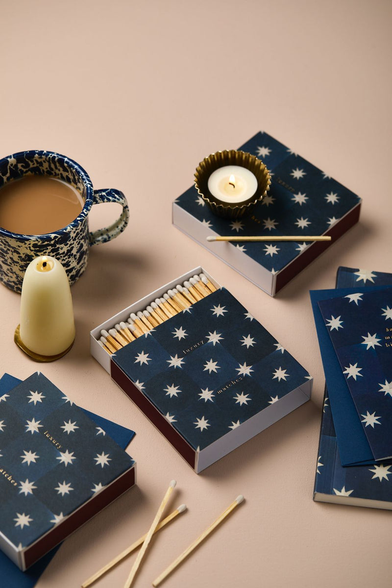 Matches, tea light candle, and star-patterned matchboxes on a beige surface