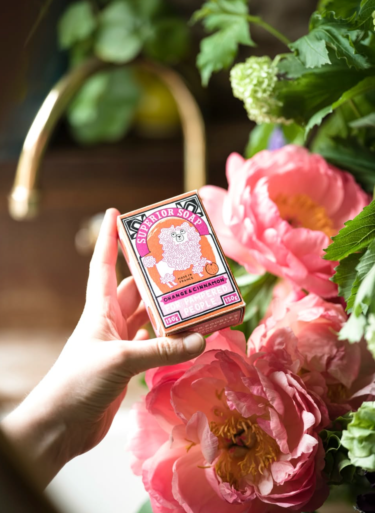 Hand holding a pink box with floral design in front of pink flowers