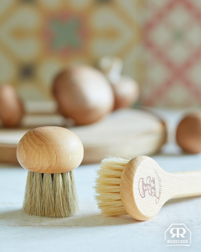 Two wooden mushroom brushes with bristle heads on a light surface, with a blurred background.