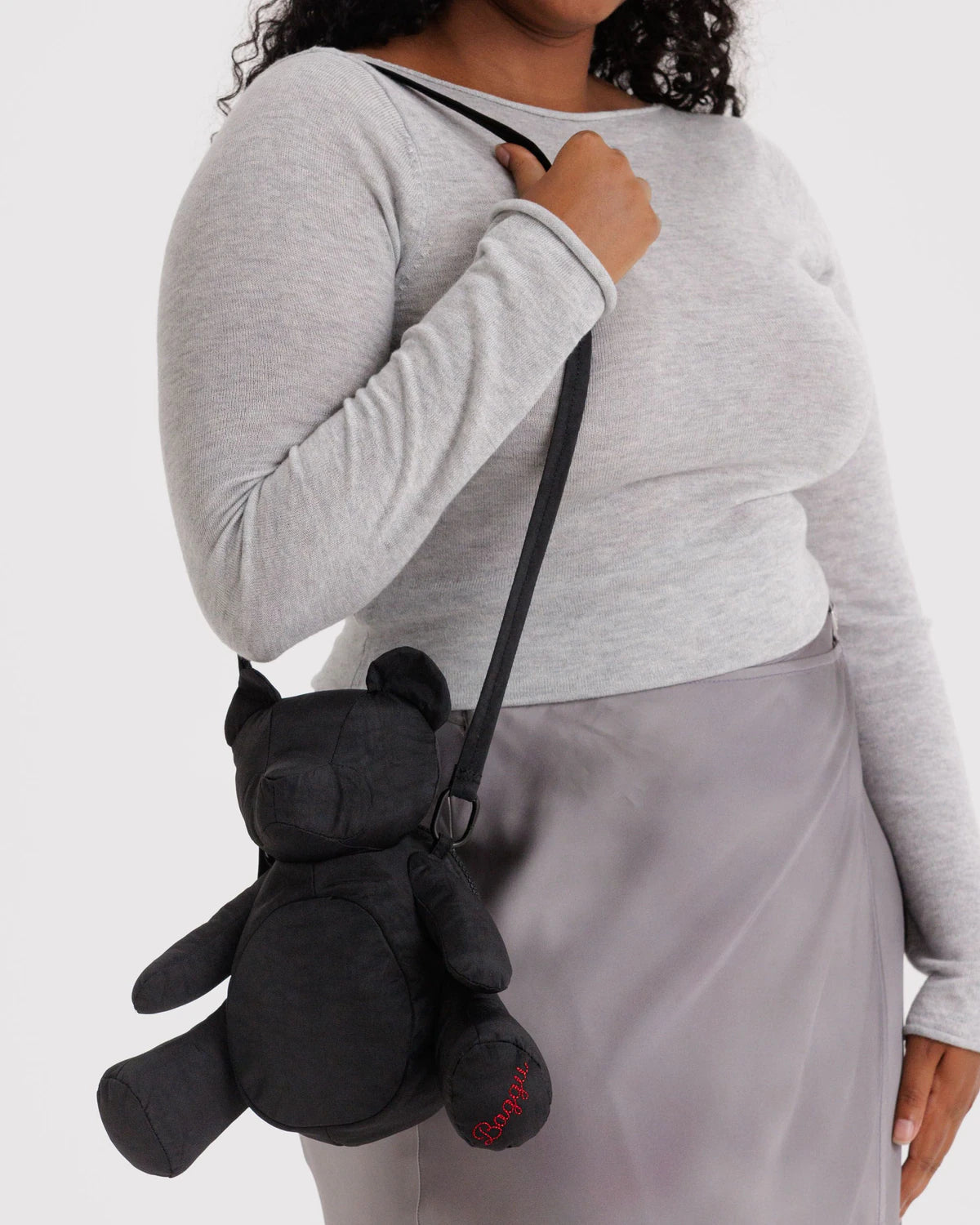 Person wearing a gray sweater and gray skirt with a black teddy bear-shaped bag over their shoulder on a white background
