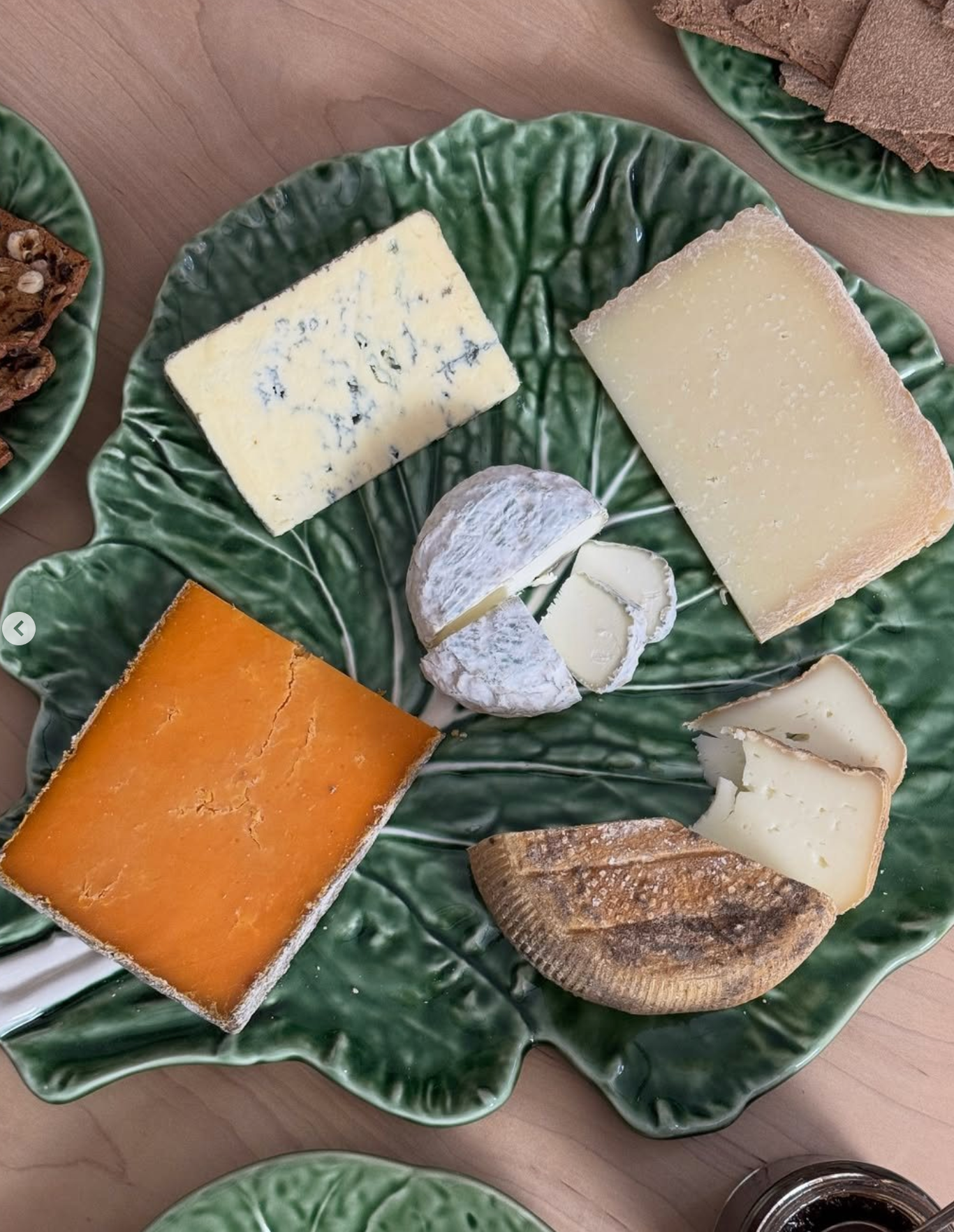 Assorted cheeses on a green ceramic plate with crackers.
