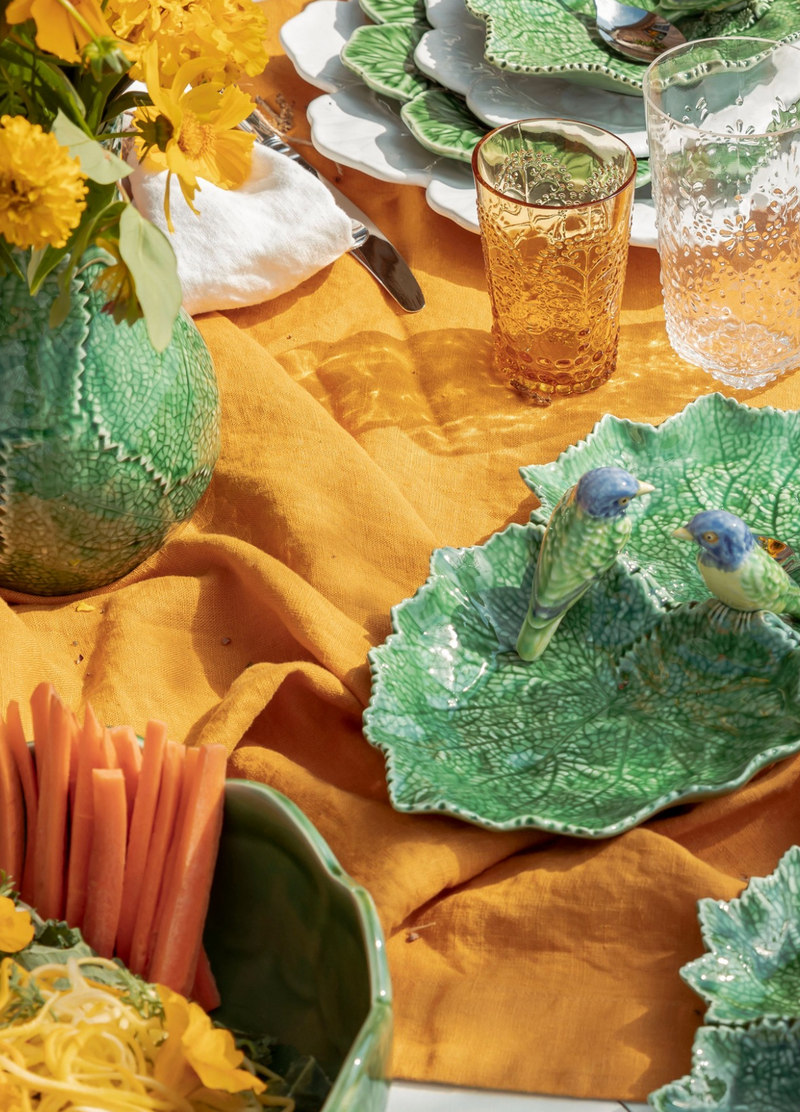 Decorative table setting with green ceramic plates, yellow flowers, and a mustard yellow tablecloth.