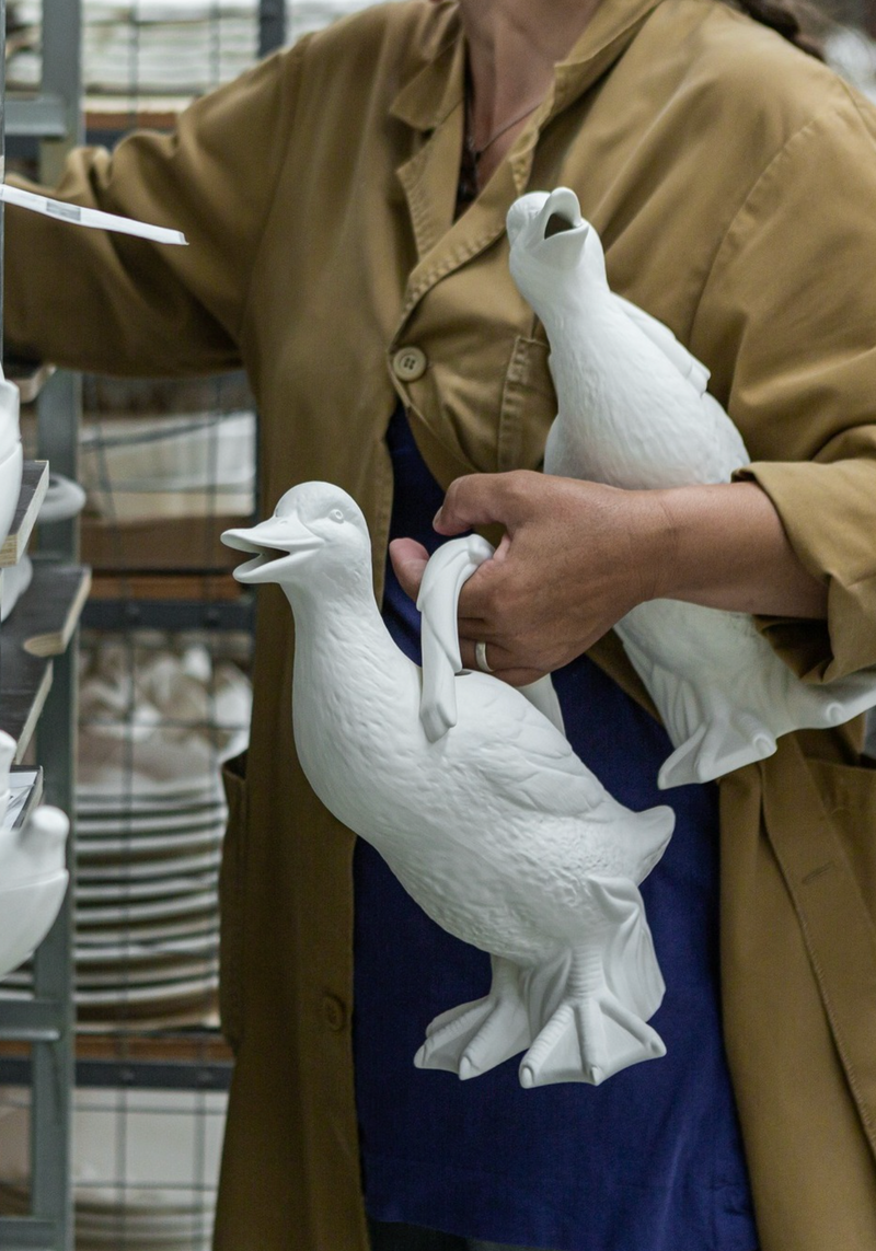 Person holding white ceramic duck pitchers in a workshop setting