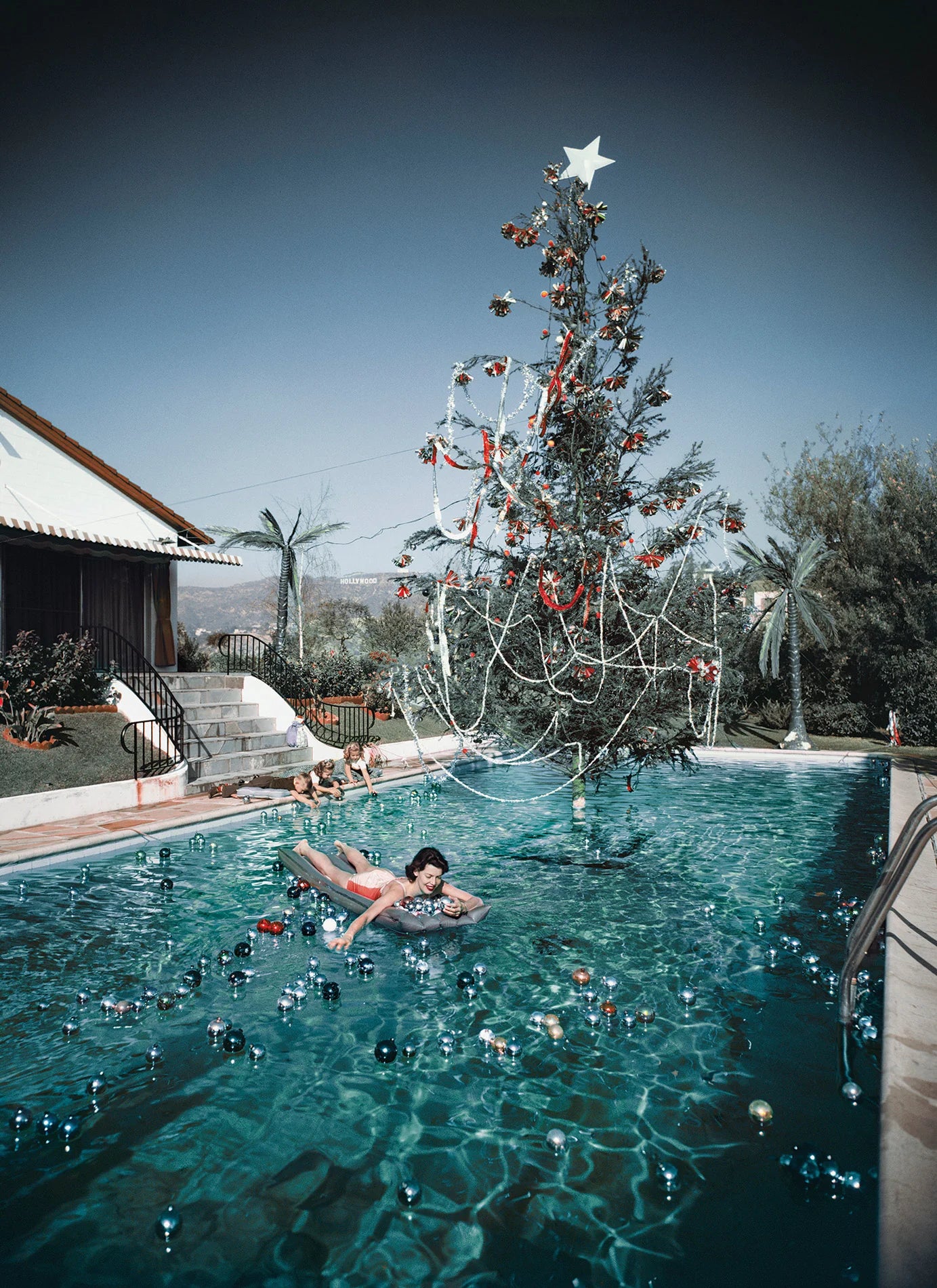 Person floating in a pool with a decorated Christmas tree in the background