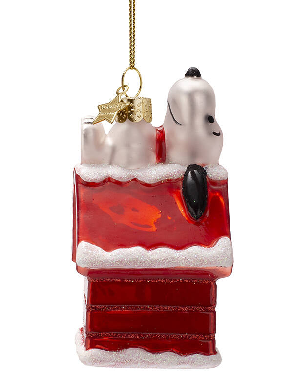 Glass ornament of Snoopy dog on a red platform with gold accents on a white background