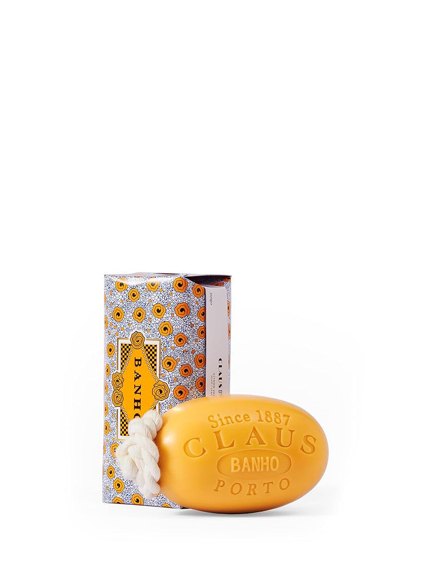 Orange soap bar with 'Claus Porto' branding next to its packaging on a white background