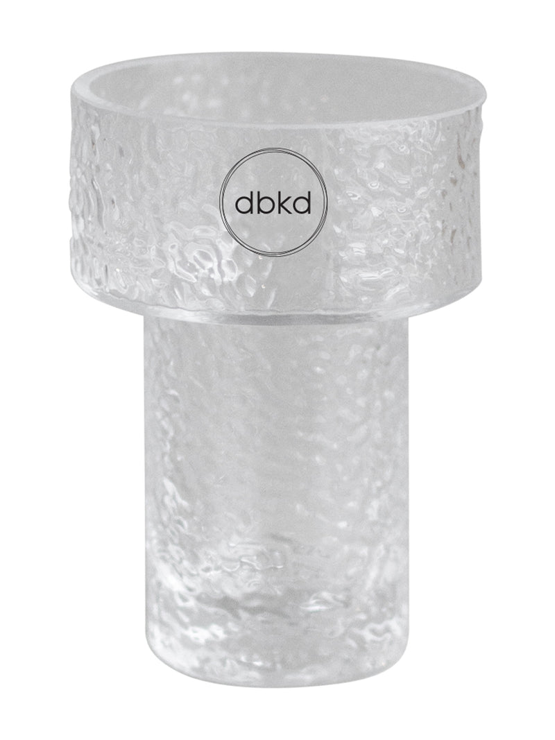 A clear textured glass vessel with a wide top rim and a cylindrical base, featuring a circular logo in the center that reads 'dbkd'.