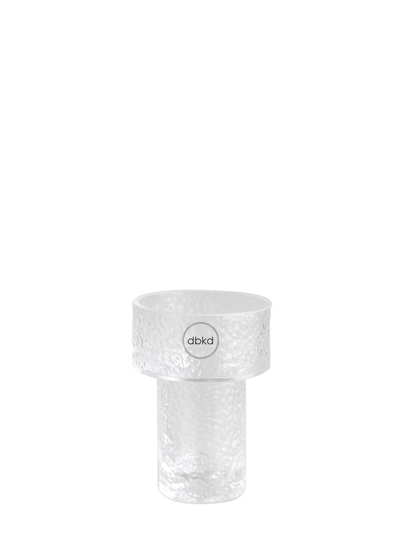A clear textured glass flowers vase with a wide top rim and a cylindrical base, featuring a circular logo sticker with the brand name 'dbkd' in the center.