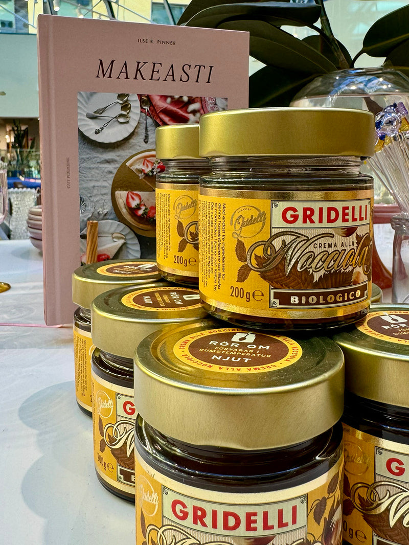Several jars of Gridelli Nutella cream and almond butter are stacked on a table, with a pink Makeasti book standing behind them in a retail or display setting.