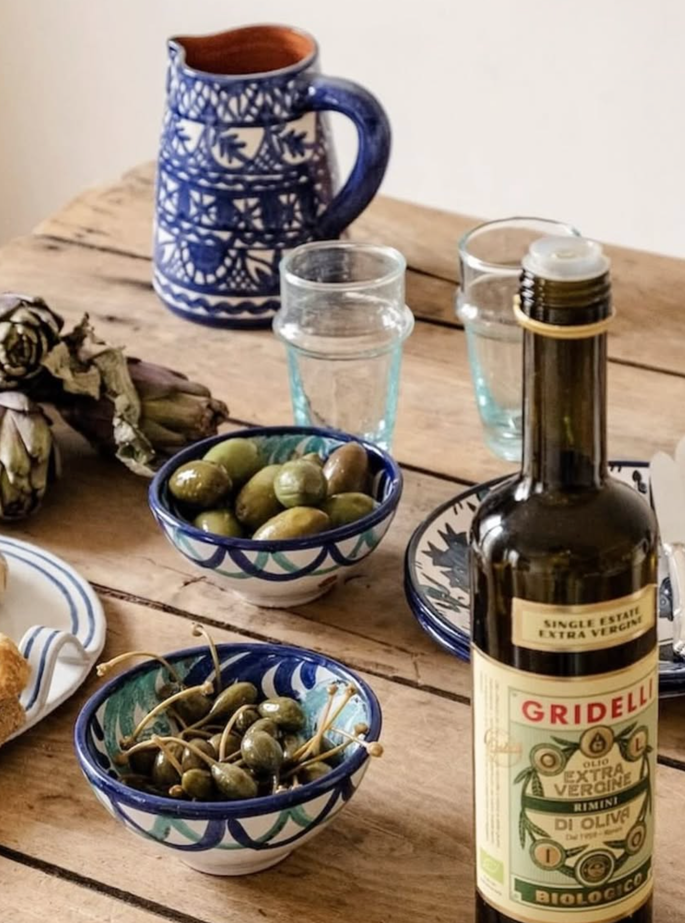 Olive oil bottle with bowls of olives and a pitcher on a wooden table