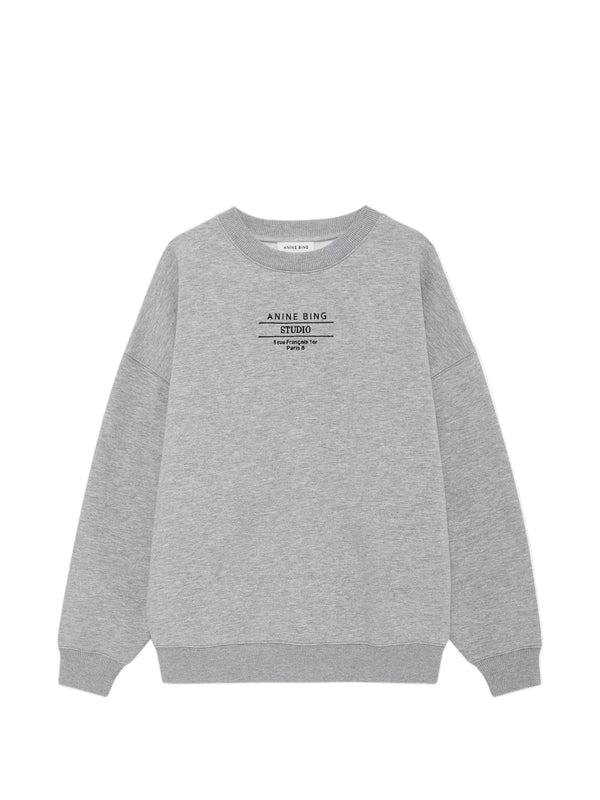 A light gray heather crewneck sweatshirt with a black graphic print on the chest reading 'ANNE RING EST.2010', displayed flat against a light gray background.