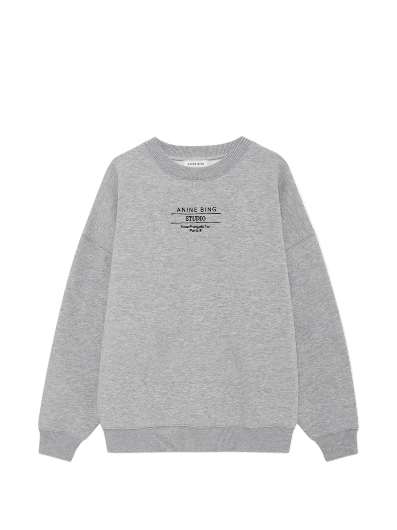 A light gray heather crewneck sweatshirt with a black graphic print on the chest reading 'ANNE RING EST.2010', displayed flat against a light gray background.