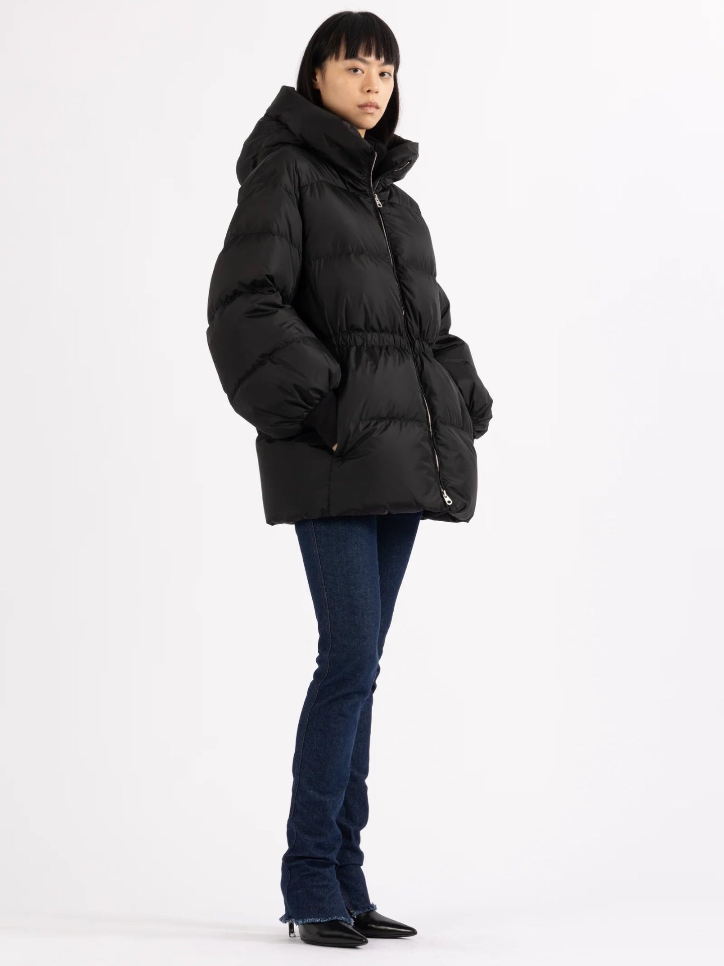 Person wearing a black puffer jacket and dark jeans on a white background