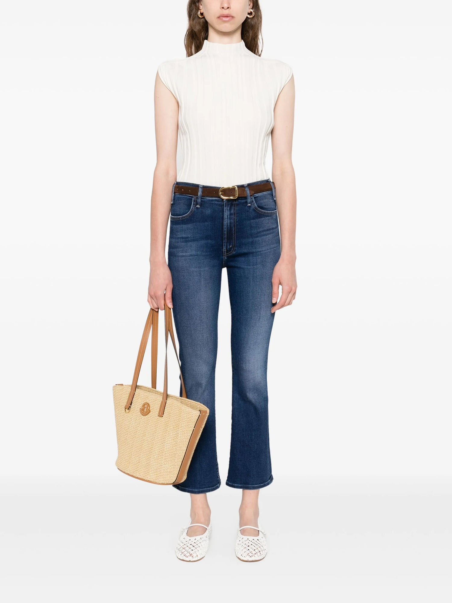 Woman wearing a white top and blue jeans, holding a beige tote bag on a white background