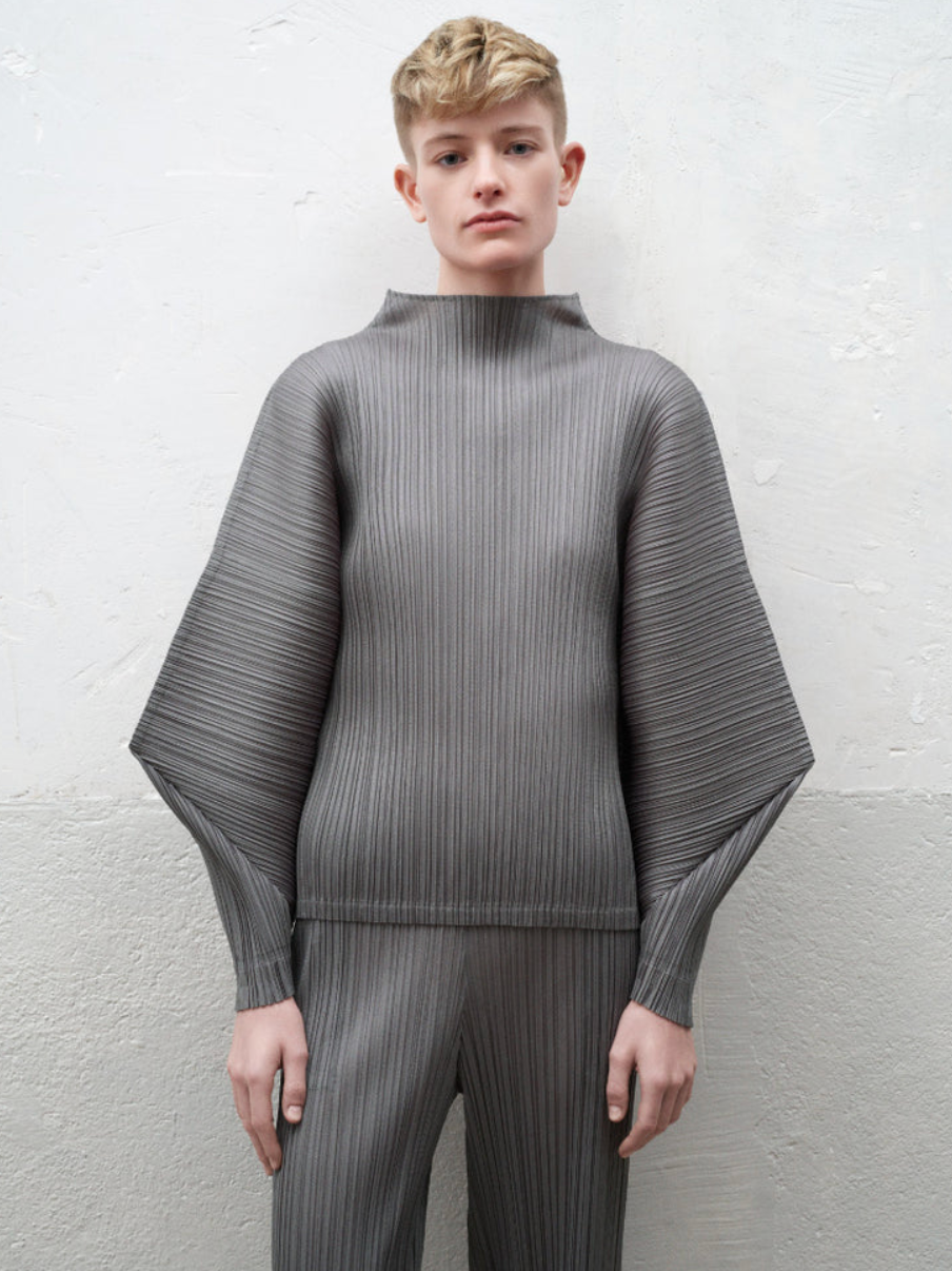 Person wearing a gray pleated sweater and pants against a white background