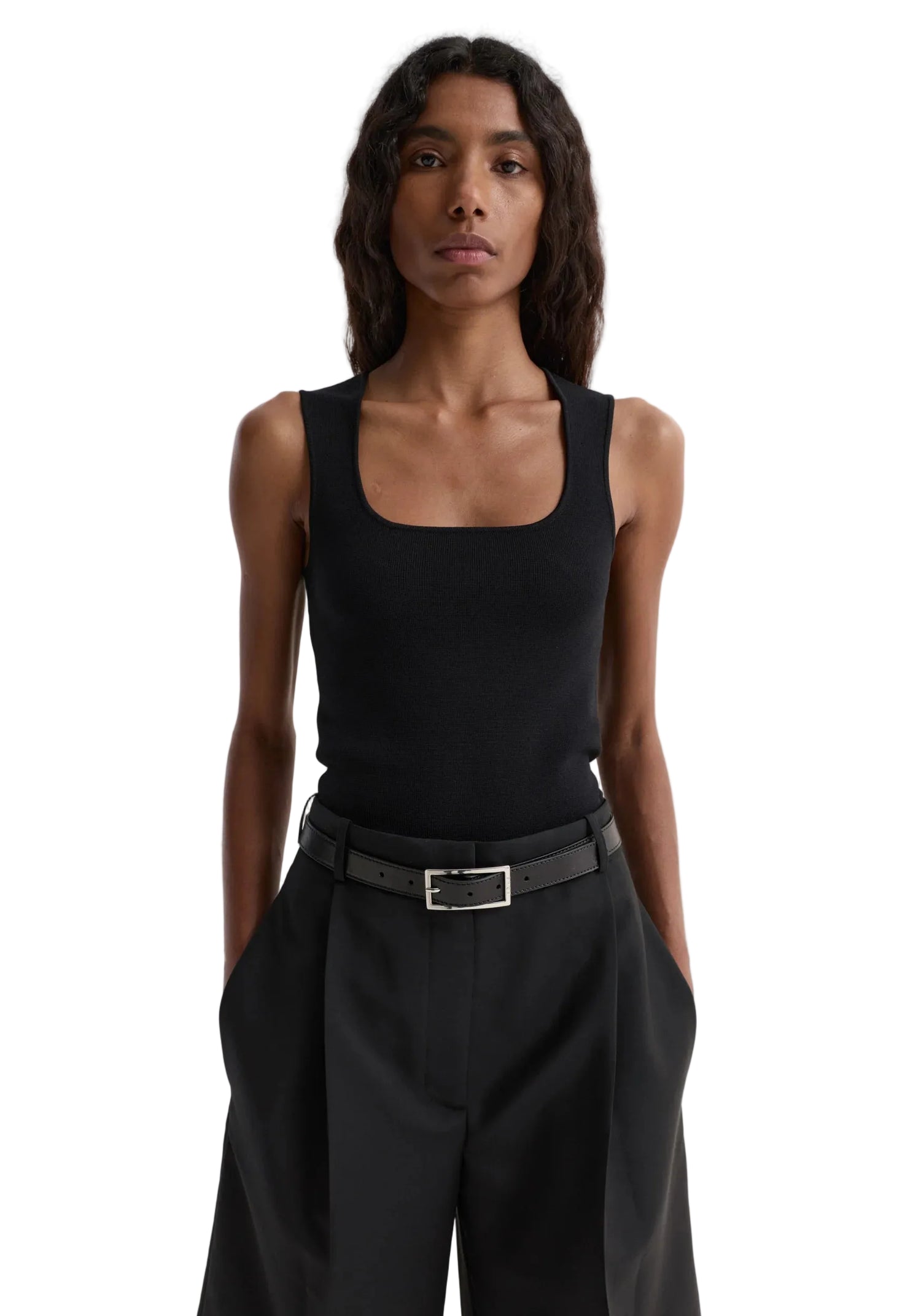Person wearing a black sleeveless top and black pants on a white background
