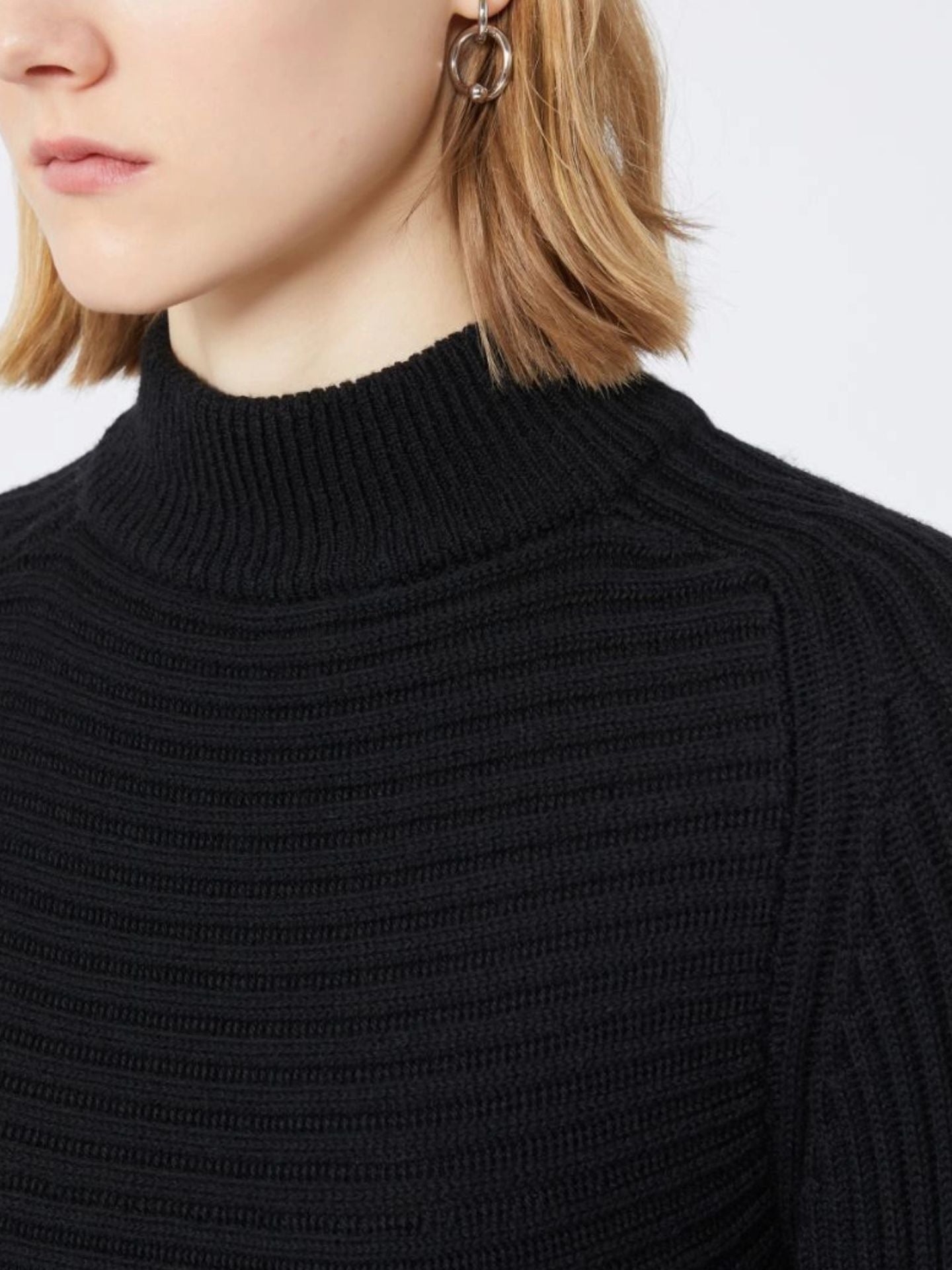 Close-up of a person wearing a black turtleneck sweater on a light background