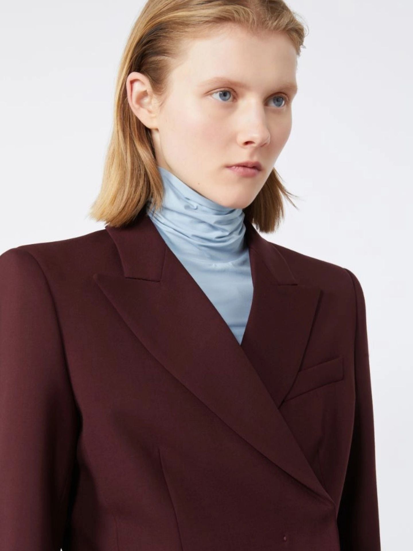 Woman wearing a burgundy blazer over a light blue turtleneck on a white background