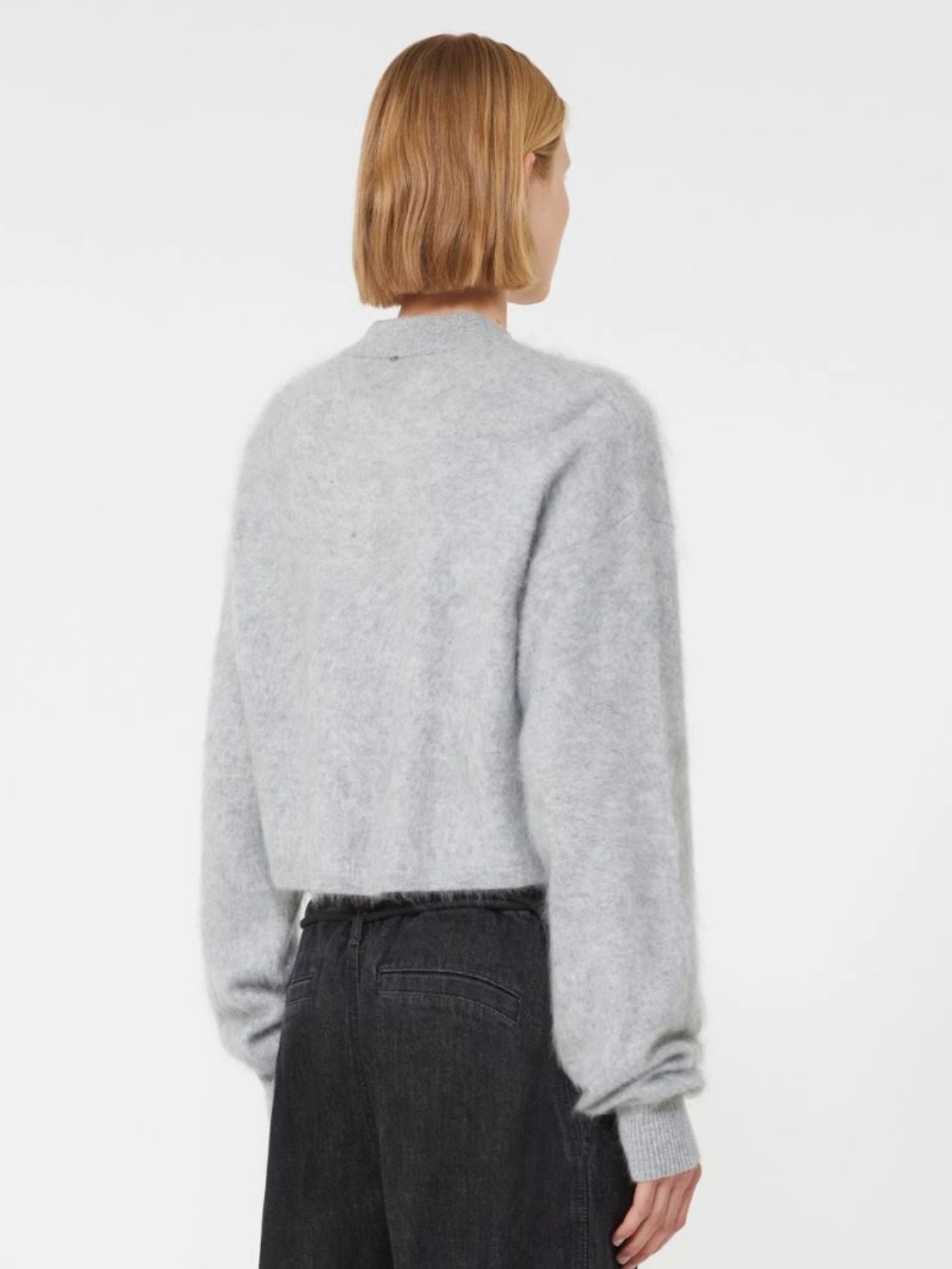 Person wearing a gray sweater and dark pants on a white background